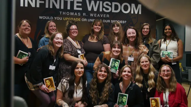 A large group of readers at the launch, in front of the Infinite Wisdom backdrop, holding up their copies of the limited edition.